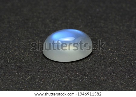 Natural adularia blue sheen oval shaped cabochon moonstone. Loose gem on gray textured leather background. Feldspar mineral group. Semiprecious gemstone not common relatively rare and expensive stone Imagine de stoc © 