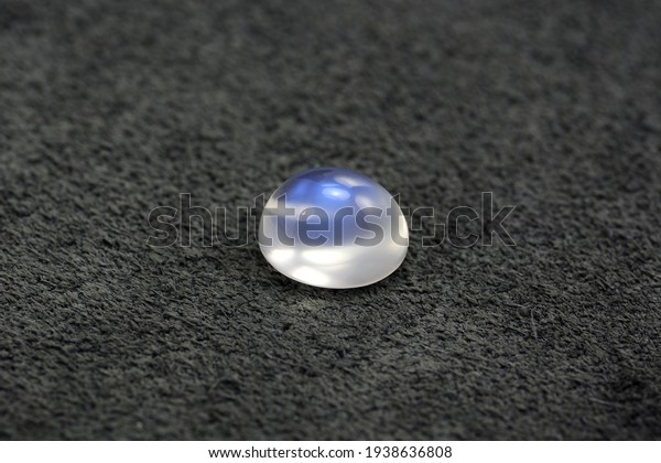 Natural adularia blue sheen oval cabochon\
moonstone. Loose gem on gray textured real leather background.\
Feldspar mineral group. Semiprecious gemstone not common relatively\
rare and expensive\
specimen
