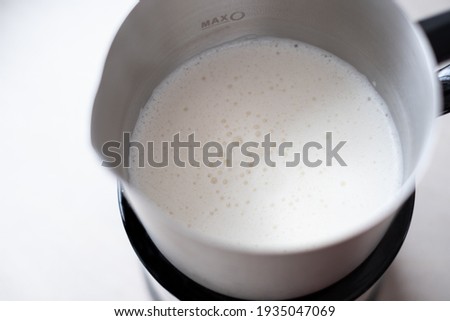 Natural almond, oat or soya mink froth. Preparing hot vegan coffee drinks. Plant-based milk foam in frother.