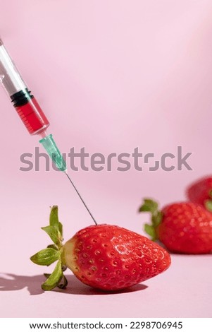 Natural and artificial food coloring. Syringe injecting artificial coloring into a fresh strawberry.