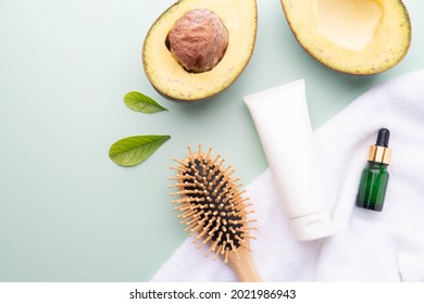 Natural Avocado Hair Products For Healthy Hair. Blank White Squeeze Tube Of Shampoo With Hair Serum Bottle, Comb, Towel And Fresh Organic Avocado On Green Background. Beauty Herbal Haircare Concept.