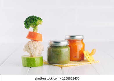 Natural Baby Food Concept. Vegetable Puree In Jars Near Pyramid Of Brocolli, Carrot, Cauliflower And Zucchini Pieces On White Background With Blank Space For Text.