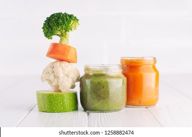 Natural Baby Food Concept. Vegetable Puree In Two Jars Near Pyramid Of Brocolli, Carrot, Cauliflower And Zucchini Pieces On White Background With Blank Space For Text.