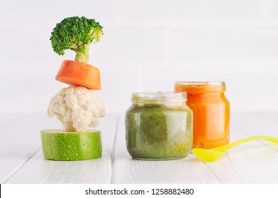 Natural Baby Food Concept. Vegetable Puree In Jars Near Pyramid Of Brocolli, Carrot, Cauliflower And Zucchini Pieces On White Background With Blank Space For Text.