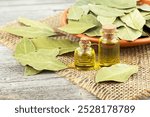 Natural bay laurel essential oil in glass bottles with dried bay leaves on a wooden table. Healthy lifestyle and beauty concept.