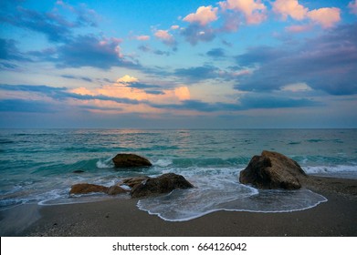 Natural beach with rocks. Clouds in the sunset.