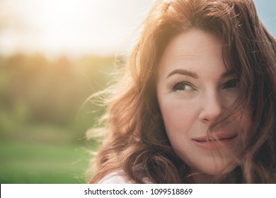 Natural Beauty. Close Up Portrait Of Dreamful Woman With Red Curly Hair. She Is Looking Aside With Enjoyment And Smiling While Resting In The Fresh Air. Copy Space 