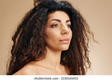 NATÜRLICHE SCHÖNHEIT KONZEPT. Profilporträt von gegerbter, bezaubernder Lateindame mit natürlichen, gesunden Curls, die einzeln auf beigem Hintergrund stehen, sieht abseits. Kosmetikangebot im Friseur