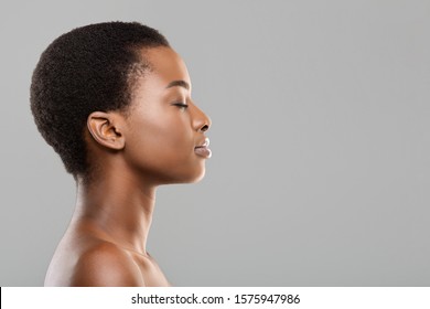 Natural beauty concept. Side view portrait of young beautiful afro woman with flawless skin standing with closed eyes over gray background, copy space