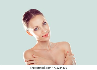 Natural beauty with flawless skin. Beautiful face young adult woman with clean fresh skin hands on shoulders, hug herself isolated light green background. Beauty light nude makeup looking slight smile