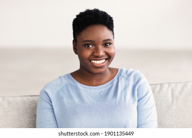 Natural Beauty. Headshot Portrait Of Casual Young Large Build Black Woman Smiling, Looking And Posing At Camera, Resting Alone On The Sofa At Home In Bedroom. Closeup Of Positive Chubby Female