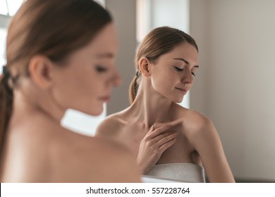 自然の美。若い女性が肌に触れ、鏡の前に立って目をそらす肩越しの眺め
