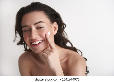 Natural Beauty Of Skin Care. Close Up Portrait Of Happy Smiling Pretty Brunette Lady Tenderly Applying Cream On Face. Isolated On White With Copy Space On Right