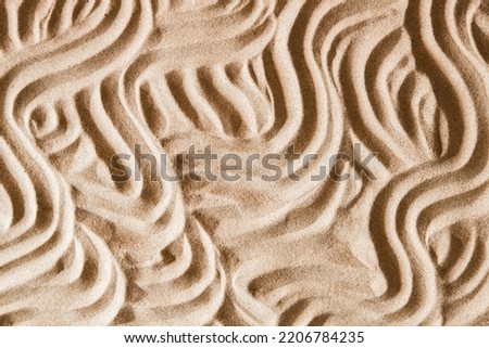 Natural beige sand texture background with wave pattern. Wavy curved ornaments on sand, drawn by hand. Top view