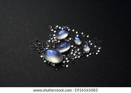 Natural blue sheen moonstones adularia oval cabochon gemstones with white round calibrated natural sapphires on dark gray, black pattern background isolated. Feldspar loose stones Imagine de stoc © 
