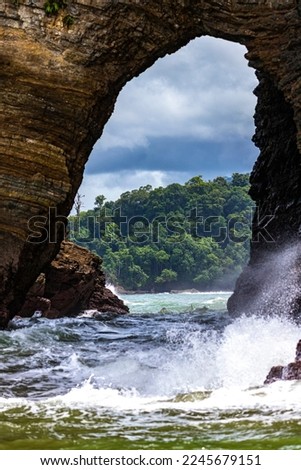 natural bridge in the rocks on the pacific coast of costa rica in marino ballena national park; view through a tunnel in the rocks to a paradise beach with palm trees	
