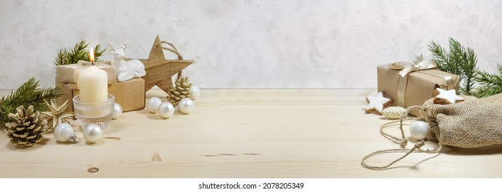 Natural Christmas decoration with a warm white candle, baubles, stars, and gifts on a wooden table against a light plastered wall, panoramic format, copy space, selected focus, narrow depth of field - Powered by Shutterstock