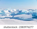 Natural cold background with huge blocks of blue transparent ice floes on snowy hummock field of frozen Baikal Lake on sunny frosty January day. Scenic winter landscape. Ice travel and outdoors