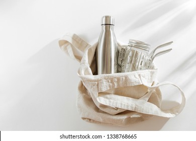 Natural color eco bag with reusable metal water bottle, glass jar and straw. Zero waste. Sustainable lifestyle concept. 