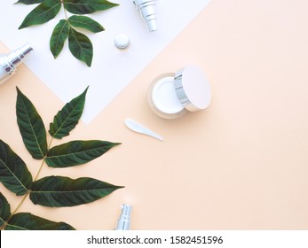 Natural Cosmetics Concept. Fresh Green Leaves, Face, Eye Cream Scrub, Shower Gel, Liquid Soap, Spa Stones On White Paper Isolated On A Beige Nude Skin Color Background. Flat Lay, Top View Copy Space. 