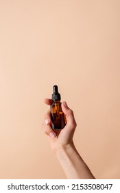 Natural Cosmetics. Dropper Bottle Mock-Up. Female Hand Holding Amber Glass Dropper Bottle On Beige Background