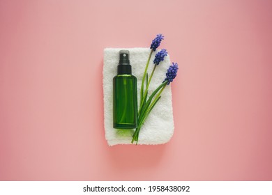 Natural Cosmetics In A Green Bottle, Blue Flowers And A Towel On A Pink Background. Spring, Body Care, Spa, Flat Lay. 