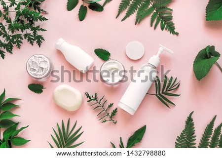 Natural cosmetics and green leaves on pink background, top view, flat lay. Natural organic skincare, bio research and healthy lifestyle concept.