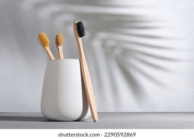 Natural eco friendly toothbrush with wooden bamboo handle in a white cup on a background with palm shadow. Zero waste lifestyle. - Powered by Shutterstock