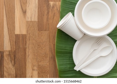 Natural eco-friendly disposable utensils (fork, spoon, dish plate, bowl and cup) made of fiber of bagasse and bamboo on green banana leaf and wooden table background with copy space. Save the earth.