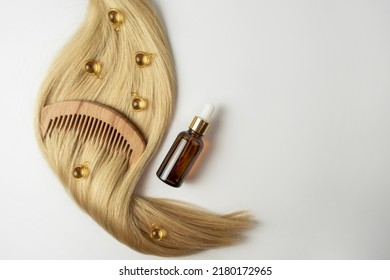 A natural essential oil or serum for hair care in golden capsules lying on a strand of  blonde hair. Hair care and smoothing concept - Shutterstock ID 2180172965