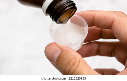 Natural expectorant syrup being placed in a graduated container to be ingested. Mention health and alternative medicine in support of the treatment of symptoms and diseases. - Shutterstock ID 2212825965