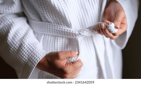 Natural fabric and closeup of female hands tying belt of white robe