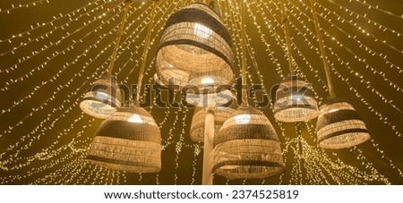 Natural fiber lamps hanging from the ceiling of a tent with a background of LED garlands. Warm atmosphere