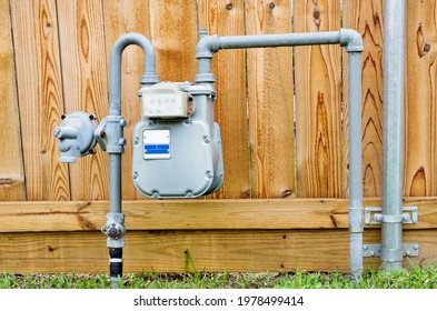 Natural gas meter in residential suburban backyard with wooden fence in background.