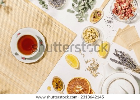 Natural healing tea from wild plants and flowers. Home herbal apothecary concept. Flat lay with dry flowers and herbs, lemon, paper tea bags, teapot and cup of tea on wooden napkin on white background