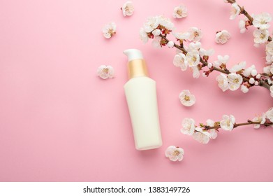 Natural herbal lotion concept. Cosmetic product bottle with apricot blossom branch on a light pink background. Blank label for branding mock-up, copy space. 