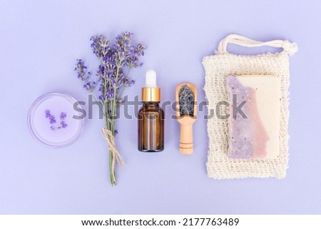 Natural herbal self-care products. Natural lavender cosmetics for home beauty treatments  - cosmetic lavender oil or face serum, organic soap and body lotion over purple background. Flat lay style