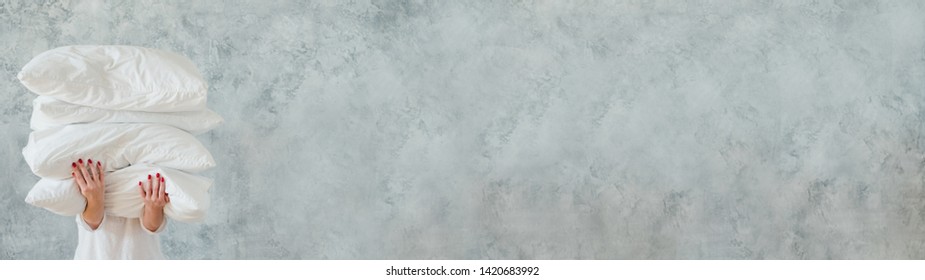Natural home textile. Woman holding big pile of white soft pillows. Gray wall background. Copy space.
