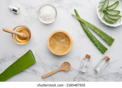 Natural Homemade Aloe Vera Gel Face And Body Scrub For Skin Problems. DIY Recipe For Sunburn, Acne And Dry Skin. Top View Of Aloe Vera, Honey, Sea Salt And Essential Oil Bottle On Marble Background.