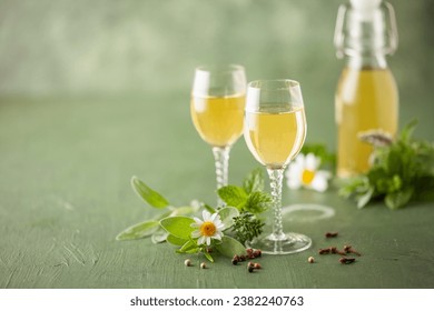 Natural homemade herbal liqueur in glasses and green leaves.