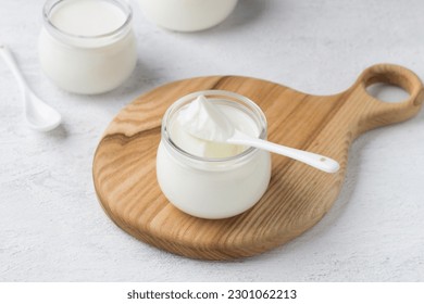 Yogur natural casero en un frasco de vidrio sobre un tablero de madera de fondo gris claro