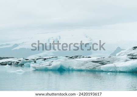 Natural Jökulsárlón Icelandic glacial lake cold blue environment with cloudy mountainous background and still clear water with icebergs 