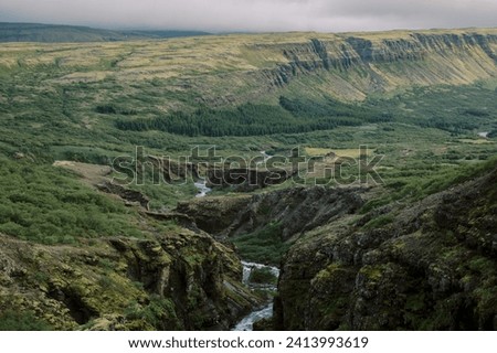 Natural Icelandic river stream coursing from Glymur waterfall through green summer countryside environment on moody cloudy day near Vik 