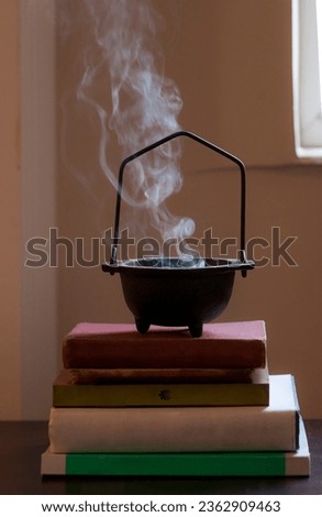 Natural incense smoke coming out of a cast iron incense burner on top of mock books  in front of a windown
