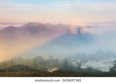 Natural landscape. Brocken Spectre in the meadow among the highest mountains in the fog and blue sky. Majestic summer scenery.