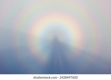 Natural landscape. Brocken Spectre in the meadow among the highest mountains in the fog and blue sky. Majestic summer scenery.