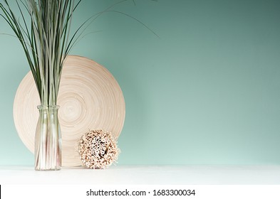 Accessoires de lumière naturelle pour la décoration maison - assiette de bambou, bouquet de roseaux en bouteille de verre, gaine ronde décorative de brindilles en menthe verte - intérieur, table en bois blanc.