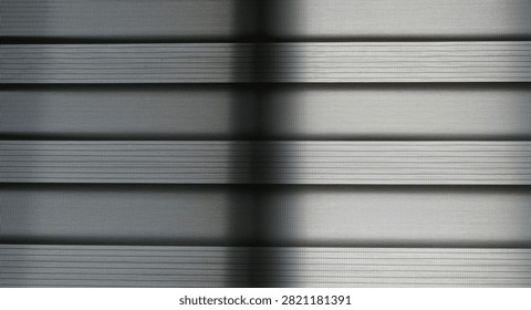 Natural light and window frame shadows on gray blinds.
Natural light passing through a window creates clean linear shadows on gray blinds. A minimalist abstract background featuring geometric lines and subtle indoor textures.