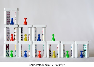 Natural lighting on a tower of dominoes with colorful game pieces of people placed in the little homes made by the dominoes. Horizontal format, white background, copy space