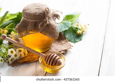 Natural linden honey. Honey in glass jar and dipper on white background with flowers.